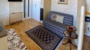 Un espace de vie compact comprenant un canapé, une petite table, un tapis à motifs et un téléviseur fixé au mur.
