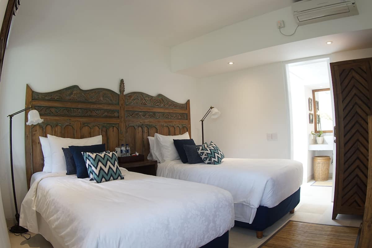 A bedroom with two beds, a wooden headboard, bedside lamps, and a door leading to another room.