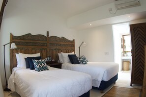 A bedroom with two beds, a wooden headboard, bedside lamps, and a door leading to another room. - Canggu Villa & Cooking Retreat (Tibubeneng)