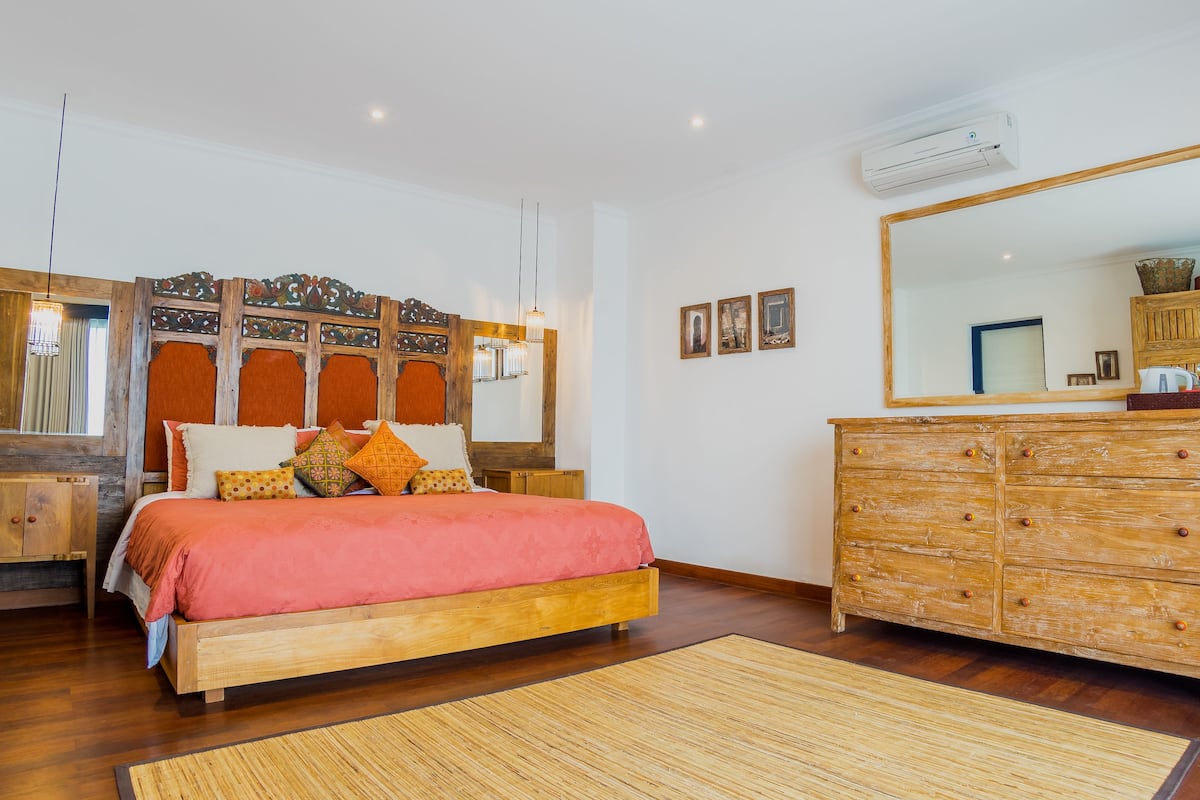 A bedroom with a wooden bed, a large mirror, a wooden dresser, and a small nightstand.