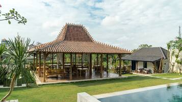 A traditional pavilion with a tiled roof, surrounded by a swimming pool and lush greenery.