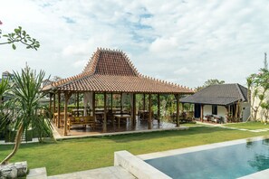 A traditional pavilion with a tiled roof, surrounded by a swimming pool and lush greenery. - Canggu Villa & Cooking Retreat (Tibubeneng)