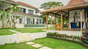 A two-story house with a tiled roof, a covered patio with furniture, and a well-maintained garden. - Canggu Villa & Cooking Retreat (Tibubeneng)