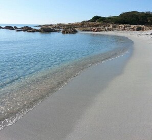 A beach with clear shallow waters, a sandy shore, and rocky outcrops in the background. - Villa Paradiso, in the beach by foot, big garden,  Wifi, all inclusive (Cala Liberotto)