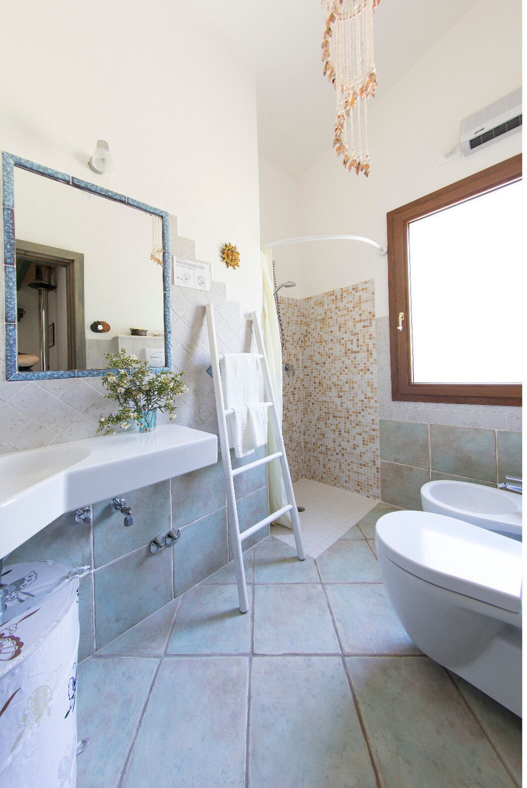 Ein Badezimmer mit Waschbecken, Spiegel, Duschbereich mit Mosaikfliesen und Toilette.