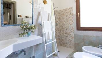 Ein Badezimmer mit Waschbecken, Spiegel, Duschbereich mit Mosaikfliesen und Toilette.