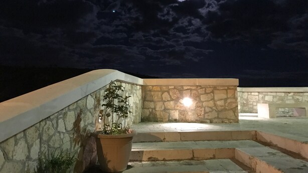 Terrassa al terrat amb una planta en test, mur de pedra i vista del cel nocturn amb núvols.
