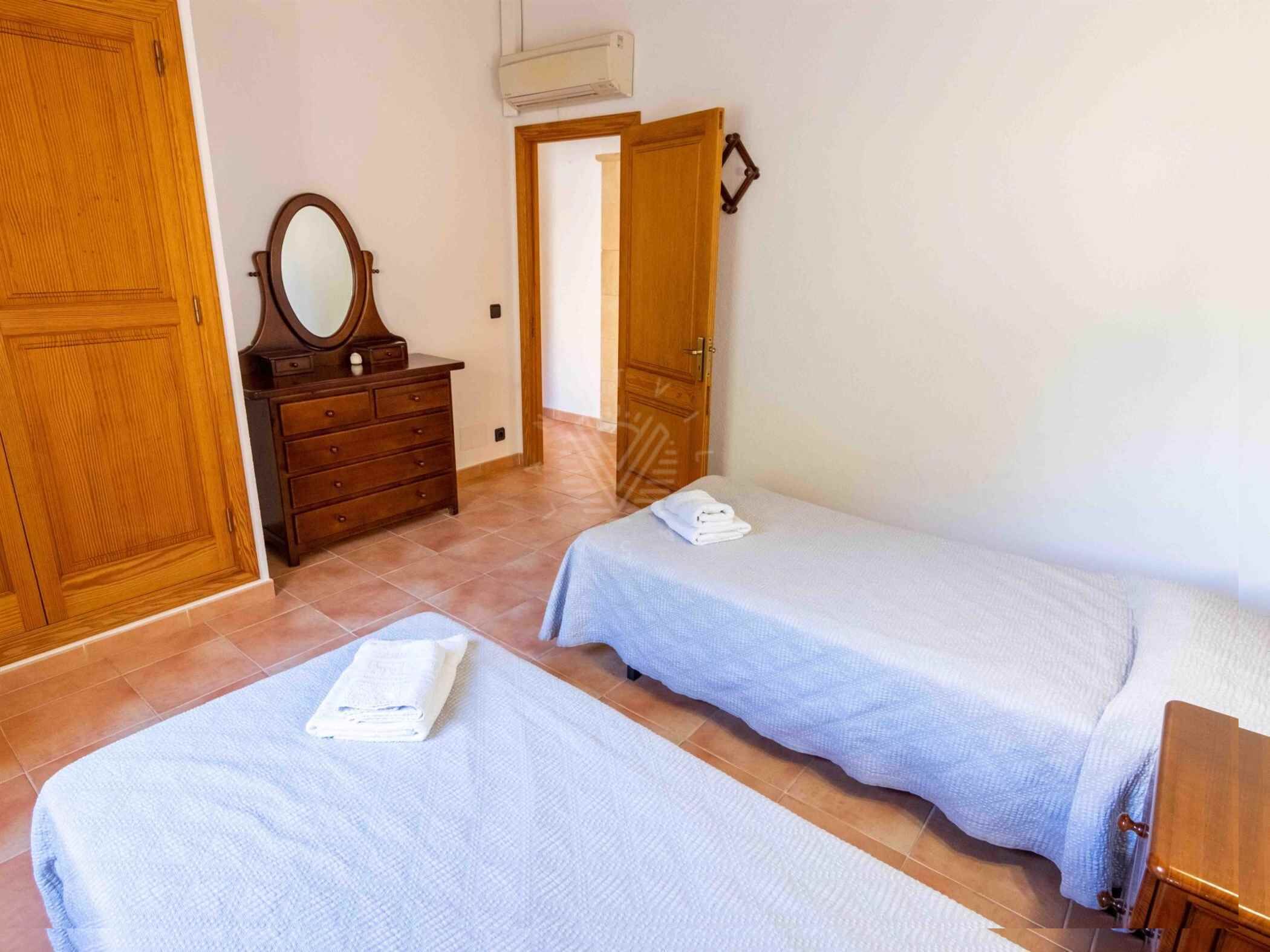 A room with two single beds, a wooden dresser with a mirror, and a door leading to another room.