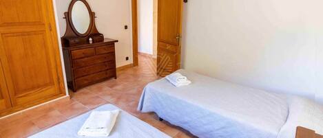 A room with two single beds, a wooden dresser with a mirror, and a door leading to another room.