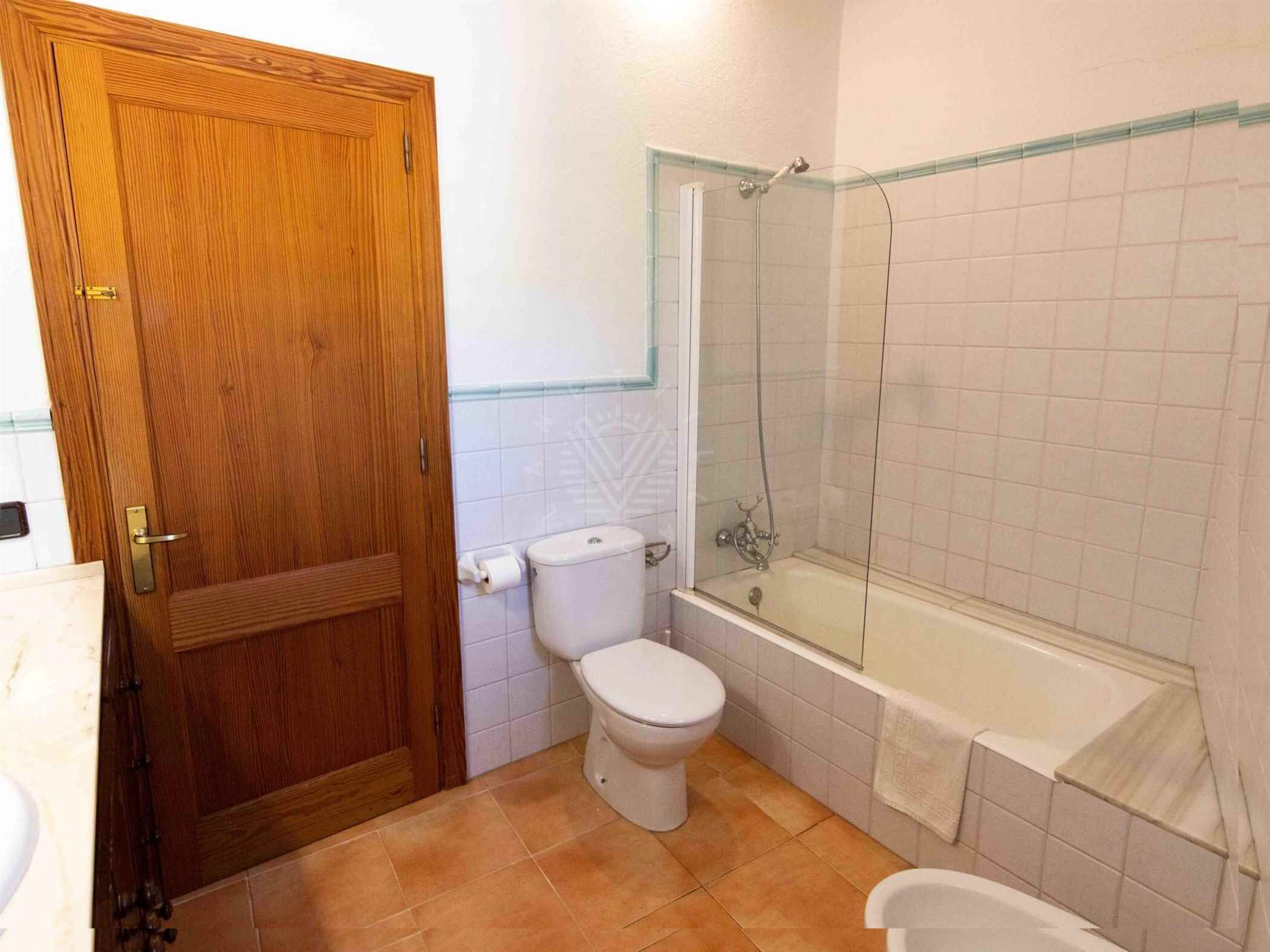 Une salle de bain avec une porte en bois, des toilettes, une baignoire et une douche à parois de verre.