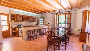 A spacious kitchen with wooden cabinets, a central island with stools, and a dining area with a large table and chairs. - Can Bajoca 2 , beautiful peaceful surroundings (Pollensa)