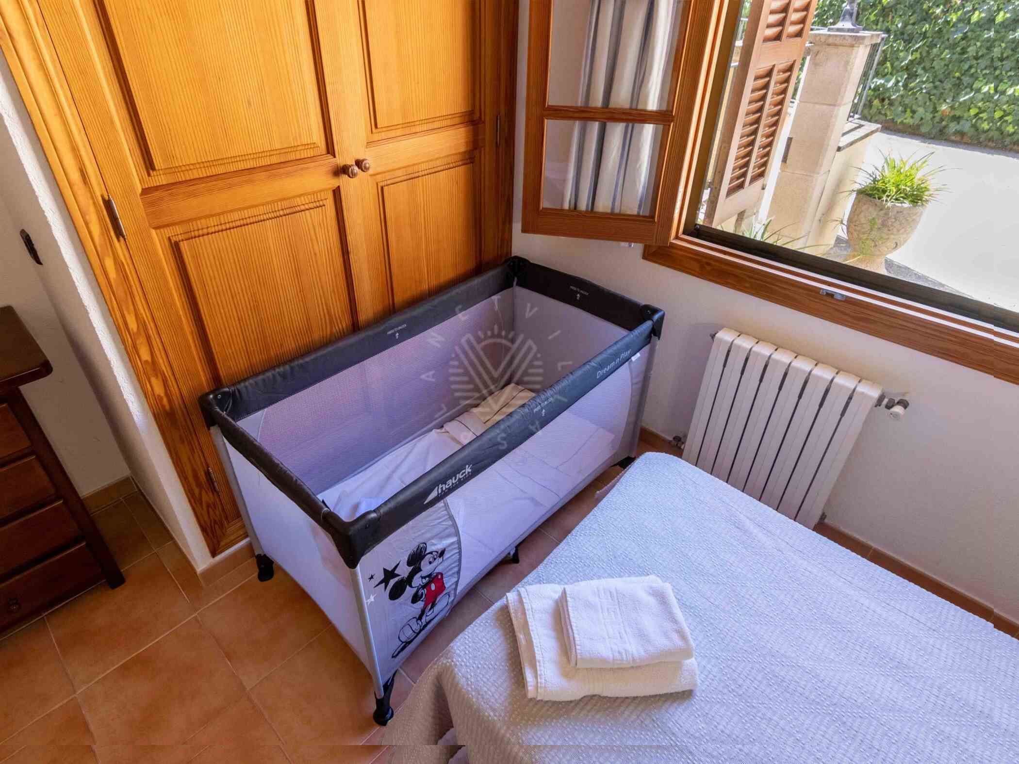 A room with a crib, a bed, a window with blinds, and a radiator.