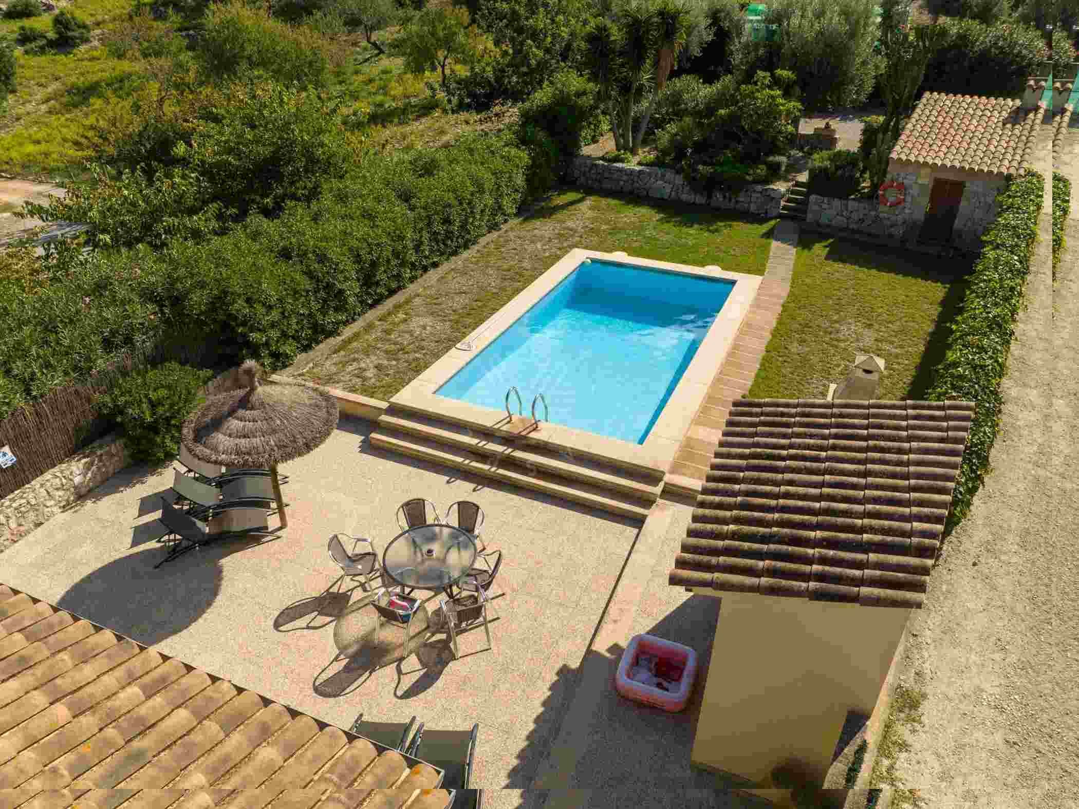 Piscina com deck ladrilhado, rodeada por vegetação e um muro de pedra.