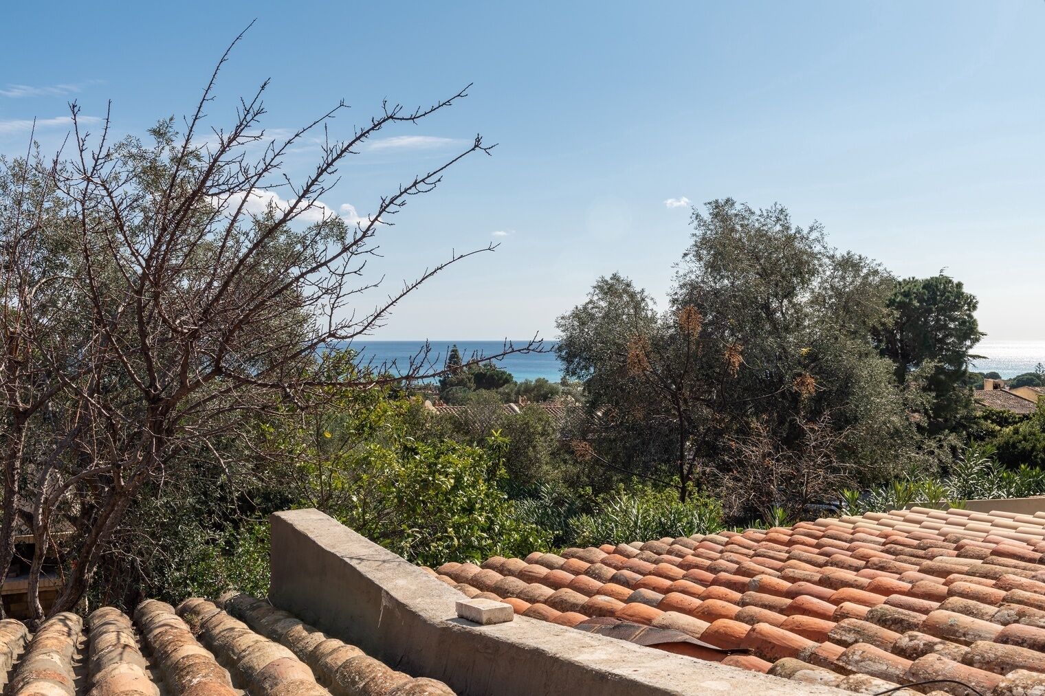 Eine Dachterrasse mit Terrakotta-Fliesen, Blick auf das Meer und umliegende Bepflanzung.