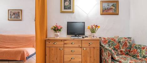 Una habitación con cama, cómoda de madera con cajones, televisor y dos cuadros en la pared.