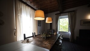 A dining area with a long wooden table, hanging pendant lights, and a view of greenery outside. - Casale Amati La Marchesa, ancient and fascinating oil mill between sea and hills. (Ortonovo)