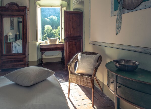 A bedroom with a bed, a wicker chair, a dresser, and a window with a view of trees.