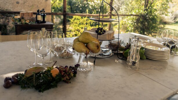 A table set outdoors with wine glasses, a fruit display, and plates. - Casale Amati La Marchesa, ancient and fascinating oil mill between sea and hills. (Ortonovo)