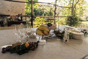 Tavolo apparecchiato all'aperto con bicchieri da vino, un vassoio di frutta e piatti.