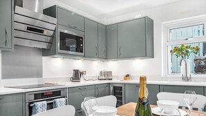 Une cuisine moderne avec des meubles gris, des appareils en acier inoxydable et un coin repas agrémenté d’une table en bois mise pour le repas.