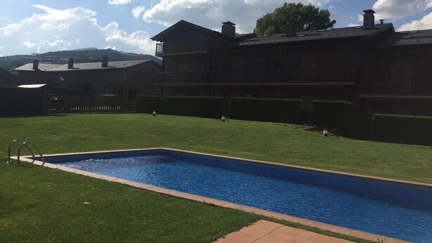 Un edificio grande con piscina, rodeado de césped cuidado y un cielo despejado.