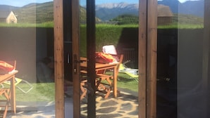 Una puerta de vidrio con marco de madera que da a un patio exterior con suelo de piedra, una mesa de madera y una silla.
