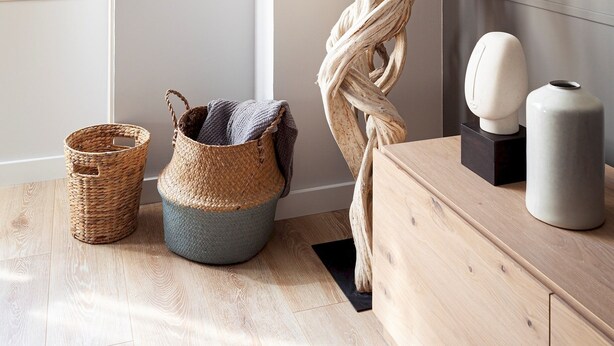 A modern room with a wooden floor, a large abstract sculpture, a woven basket, and a small round table with a vase.
