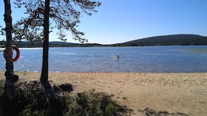 A beach with a lifebuoy on a tree, calm water, and a distant hill. - Traditional Ski Cabin in lovely forest setting in Äkäslompolo, Ylläs (Kolari)