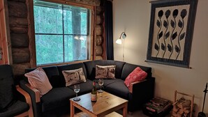 A cozy log cabin interior with a dark-colored sofa, a wooden coffee table, and a window with blinds. - Traditional Ski Cabin in lovely forest setting in Äkäslompolo, Ylläs (Kolari)