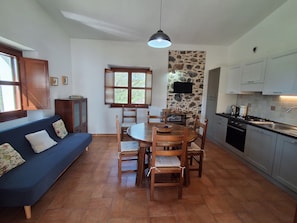 A compact kitchen with a dining table, chairs, a built-in oven, and a stone accent wall. - Sa Carruba - Typical rural house surrounded by greenery with panoramic views (Dorgali)