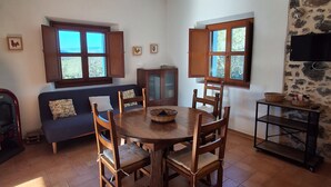 Un espace repas comprenant une table ronde en bois, des chaises, un luminaire au plafond et un mur en pierre.