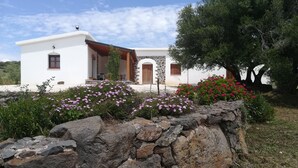 Un bâtiment blanc avec une façade en pierre, une porte en bois et un mur de pierre au premier plan.