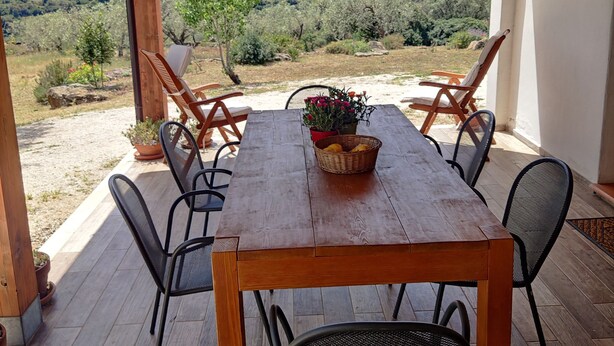 Une table en bois, entourée de chaises, placée sous une pergola en bois, d’où l’on peut admirer un paysage montagneux.