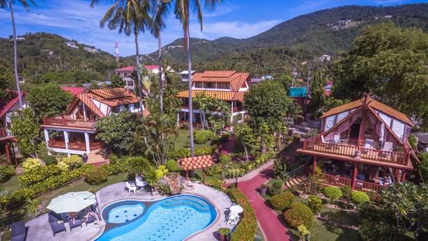 A resort with a swimming pool, multiple buildings with red-tiled roofs, and lush greenery.