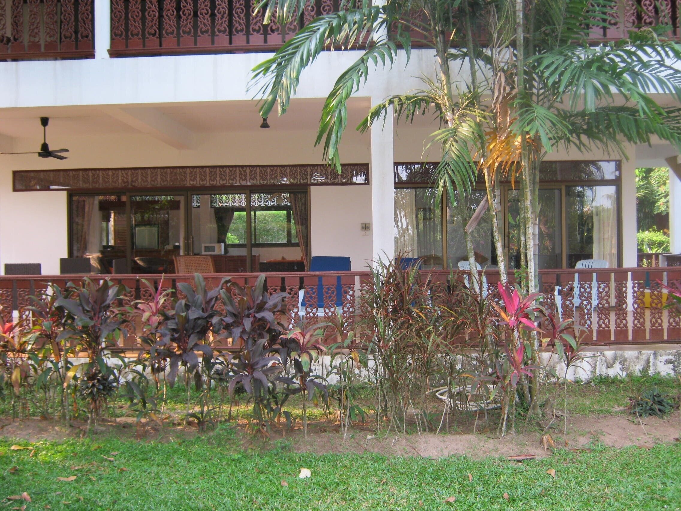 A hotel with a covered outdoor seating area, a pool, and lush greenery.