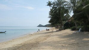A sandy beach with palm trees, a small hut, and a boat in the water.