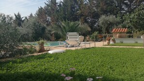 Um quintal com piscina, espreguiçadeiras e diversas plantas e árvores.