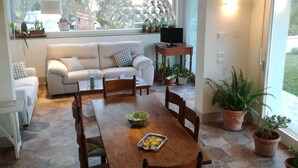 Uma sala de jantar com mesa e cadeiras de madeira, um sofá e plantas em vasos.