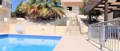 A swimming pool with a clear blue water, a palm tree, and a building with a balcony.
