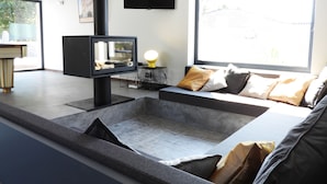 Ein modernes Wohnzimmer mit einem an der Wand befestigten Flachbildfernseher, einer Couch mit Kissen, einem Couchtisch und einem Fenster mit Blick ins Freie.