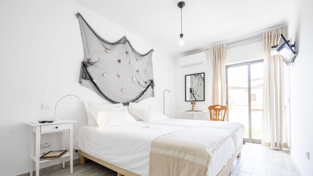 A bedroom with a bed, a nightstand, a chair, a large abstract artwork on the wall, and a window with curtains.