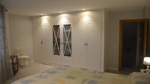 Ein Schlafzimmer mit großem Kleiderschrank, einem Sessel und einem Bett mit Blumenmuster.