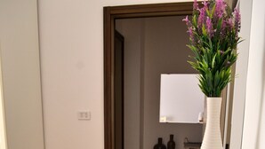 Une table blanche avec un magazine, deux bougies vertes, un bol en verre transparent et un vase blanc contenant des fleurs violettes.