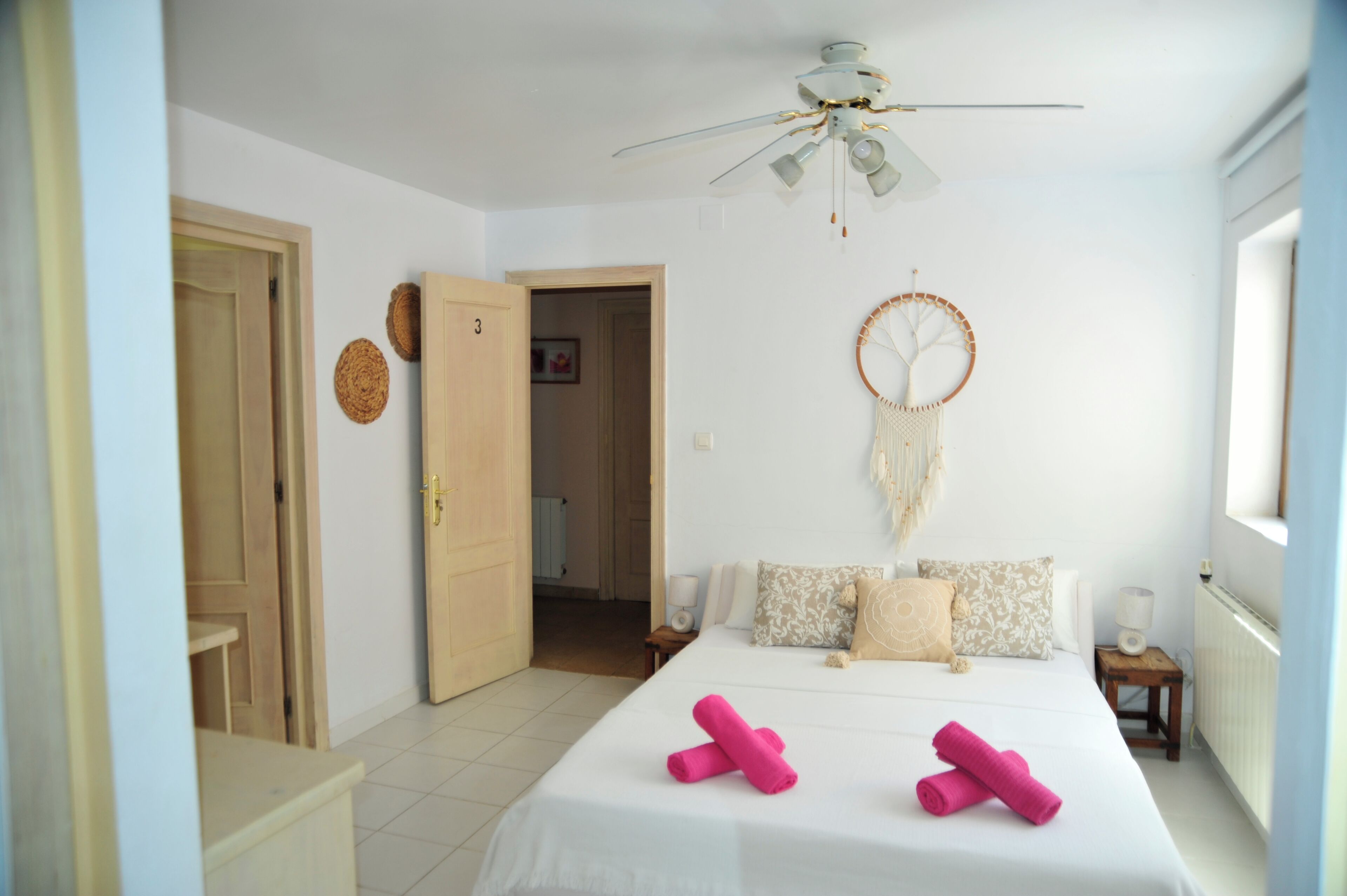Une chambre à coucher avec un lit, un ventilateur de plafond, un attrape-rêves et une porte donnant sur une autre pièce.