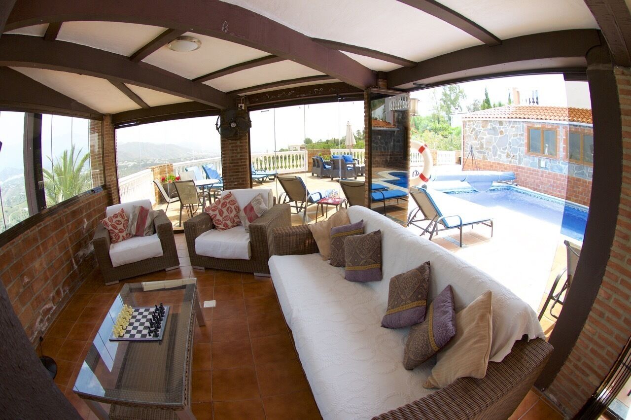 Area relax esterna coperta con piscina, mobili in vimini e una scacchiera.