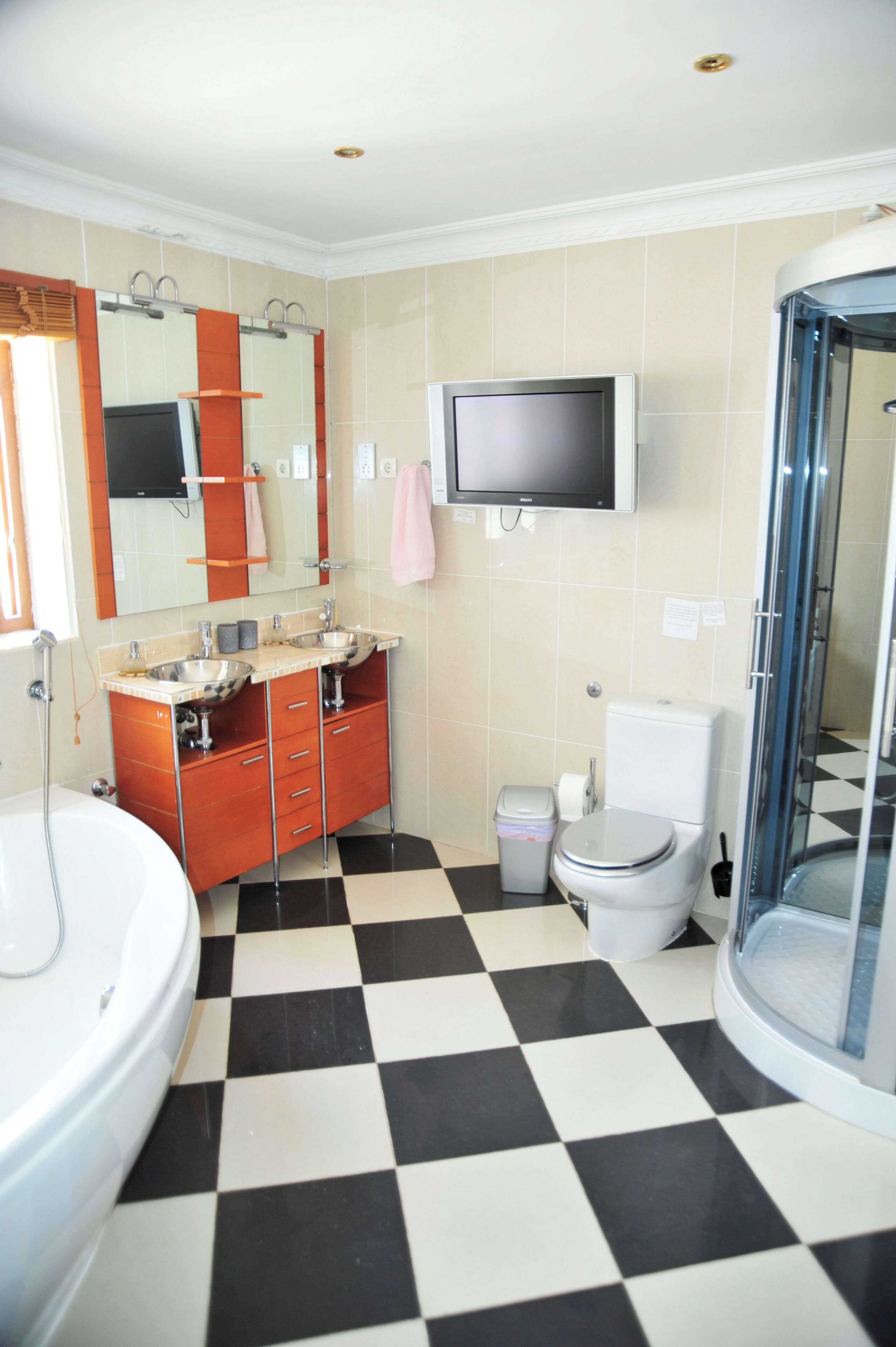 A bathroom with a checkered floor, a toilet, a sink with a mirror, a shower, and a television mounted on the wall.