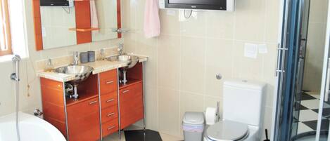 A bathroom with a checkered floor, a toilet, a sink with a mirror, a shower, and a television mounted on the wall.