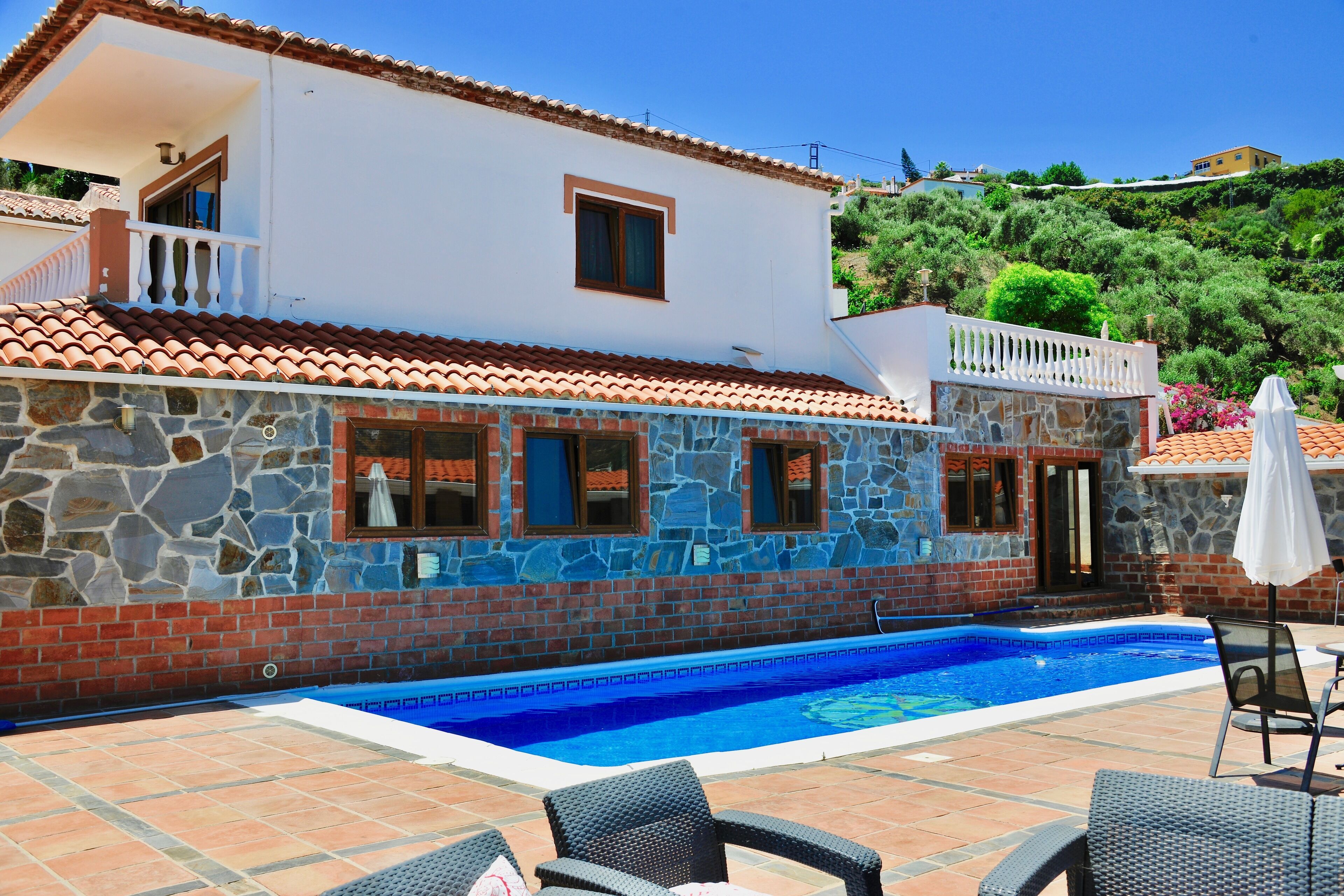 A house with a swimming pool, stone and brick exterior, and a balcony.