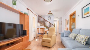 Een woonkamer met een televisie, bank en fauteuil. Er is een trap die naar een andere kamer leidt.