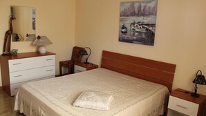 Ein ordentlich eingerichtetes Schlafzimmer mit einem großen Bett, einem Schminktisch, einem Nachttisch, einem Sessel und einem Bild an der Wand.